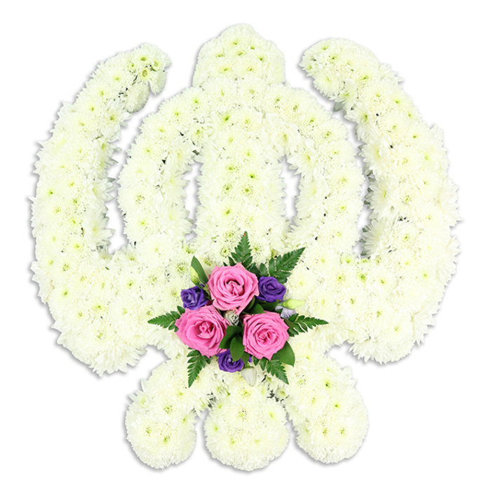 A dignified Khanda-shaped floral tribute fills the frame, its sacred Sikh symbol rendered entirely in soft white blossoms that glow gently against a plain white background. The central vertical sword rises clean and straight, bordered on each side by the perfect circular sweep of the chakkar, while the twin kirpans curve outward and down, their blades defined not by metal but by banks of densely packed chrysanthemum florets. Each flower is small and full, with overlapping petals that create a plush texture reminiscent of freshly fallen snow. Subtle shifts between ivory and warm cream add quiet depth, while the even lighting ensures every contour of the Khanda remains clearly visible. At the point where the crossed swords meet, a compact accent arrangement offers a tender counterpoint to the purity of the white. Three pink roses, at that ideal stage between bud and full bloom, present layered rosettes of silky petals, their centres a deeper rose and their outer edges softening toward blush. Tucked around them are clusters of deep purple flowers - perhaps lisianthus or freesia - whose saturated colour adds a solemn, jewel-like richness. Sprays of dark green fern fronds and glossy leaves fan gently outward, softening the lines and linking the piece back to the natural world. A light shadow beneath the tribute grounds it, suggesting it rests carefully on a stand or table. Crafted with the steady care of an experienced North London florist, this bespoke design feels perfectly suited to Sikh funeral services and memorial gatherings around Finsbury Park, Manor House, and the surrounding community, symbolising honour, spiritual strength, and everlasting remembrance.